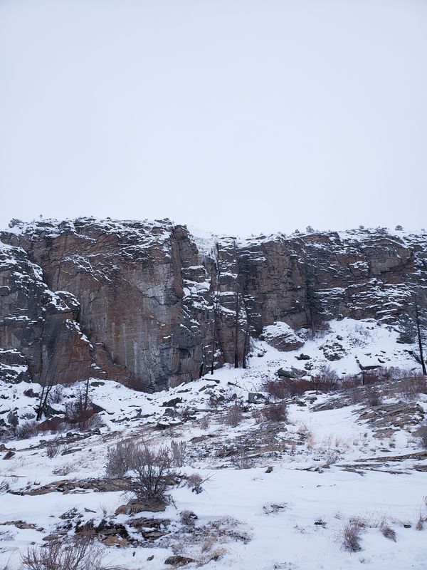 Snow-dusted gneiss cliff face at McLaughlin Canyon showing dark amphibolite bands contrasting with lighter gneiss